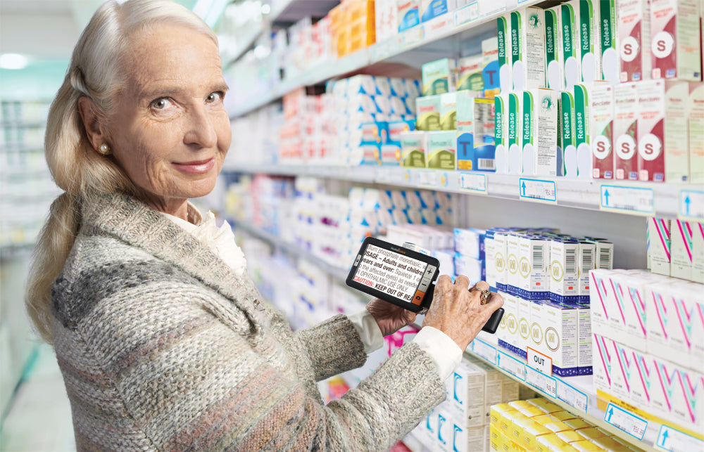 Eine ältere Dame nutzt die elektronische Lupe explore 5 beim Einkaufen in der Drogerie; VisiAid - Sehhilfen.